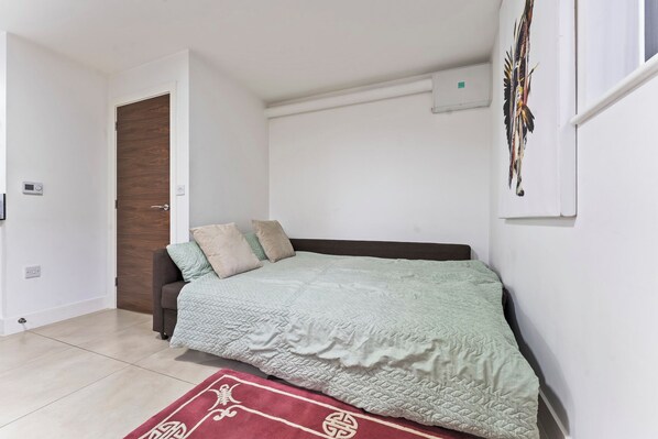 Une chambre à coucher avec un lit, une porte, un climatiseur fixé au mur et une fenêtre avec un rideau.