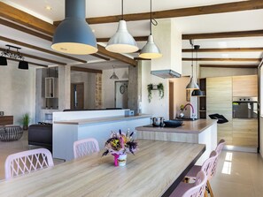 A modern kitchen with a central island, pendant lighting, and a dining area with pink chairs. - Villa Nikolina by Interhome (Pula/Banjole)