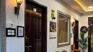 A hotel lobby with a wooden door, wall-mounted light fixtures, a calendar, and a potted plant. - Shri Ladli Stays Inn (Vrindavan)