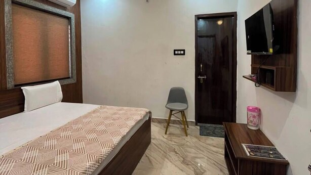 A hotel room with a bed, a ceiling fan, a TV mounted on the wall, and a marble floor. - Shri Ladli Stays Inn (Vrindavan)