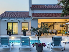 A pool area with lounge chairs, a potted plant, and a building with a tiled roof. - Villa Eva by Interhome (Pula/Banjole)