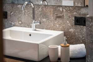 A bathroom with a white sink, a faucet, a cup, and a towel. - Knöspele Brennerei & Genuss-Apartments Vinum. (Brixen)