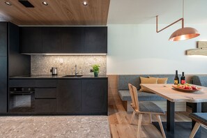 A modern kitchen with dark cabinetry, a marble backsplash, and a built-in oven. - Knöspele Brennerei & Genuss-Apartments Vinum. (Brixen)