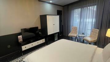A hotel room with a large bed, a TV, a wardrobe, two chairs, and a chandelier.