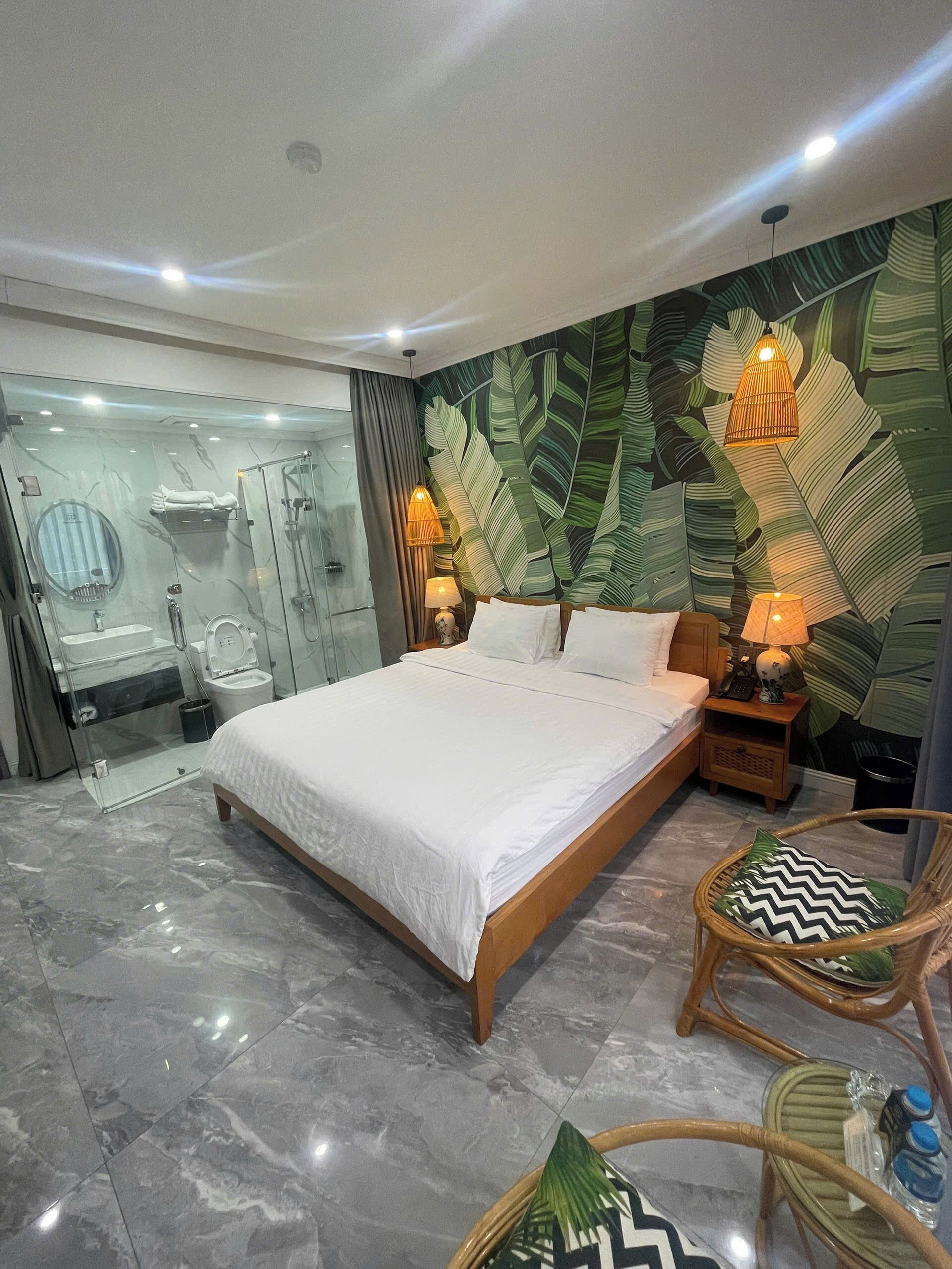 Un dormitorio moderno con una cama grande, una ducha con cerramiento de vidrio y una pared con diseño de hojas.