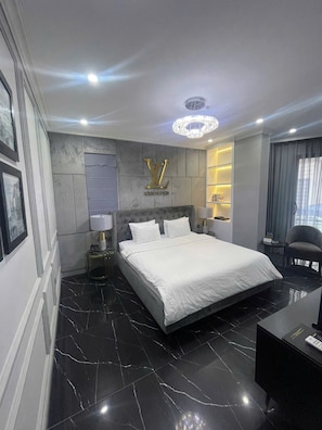 A modern hotel room with a large bed, a Louis Vuitton logo on the wall, a chandelier, and a desk with a lamp.