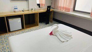 A hotel room with a bed, a desk with a chair, a television, a mirror, and a window with curtains.