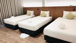A hotel room with three beds arranged in a row, each with a pillow and a towel.