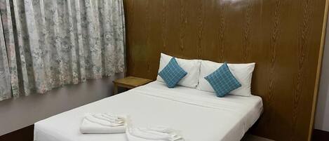 Habitación de hotel con una cama grande, cabecera de madera, mesita de noche y ventana con cortinas.