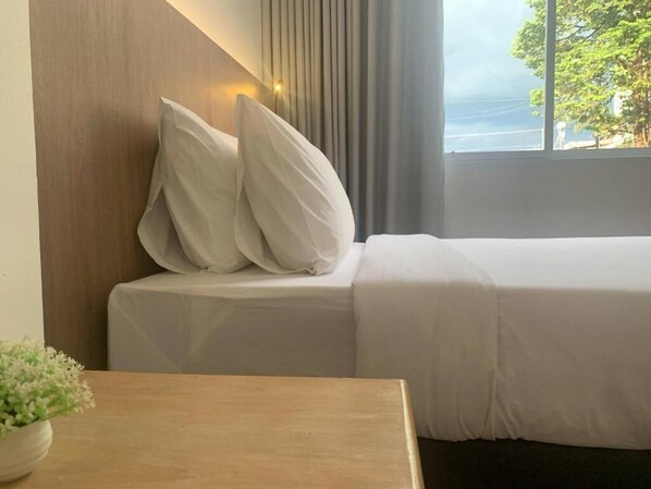 A hotel room with a bed, a bedside table with a plant, and a window with a view of the sea.
