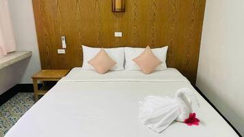 A hotel room with a wooden headboard, a bed with white bedding, two pink pillows, and a white towel with a flower on the bed.