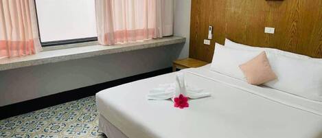 Una habitación de hotel con cama, mesita de noche, ventana con cortinas y piso estampado.