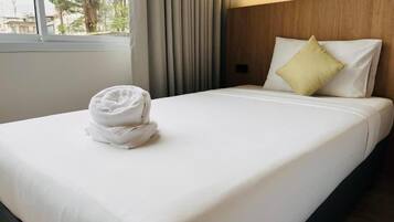 A neatly made bed with a folded towel, a wooden headboard, and a window with curtains.