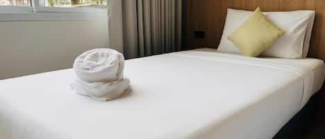 Una cama bien hecha con una toalla doblada, un cabecero de madera y una ventana con cortinas.