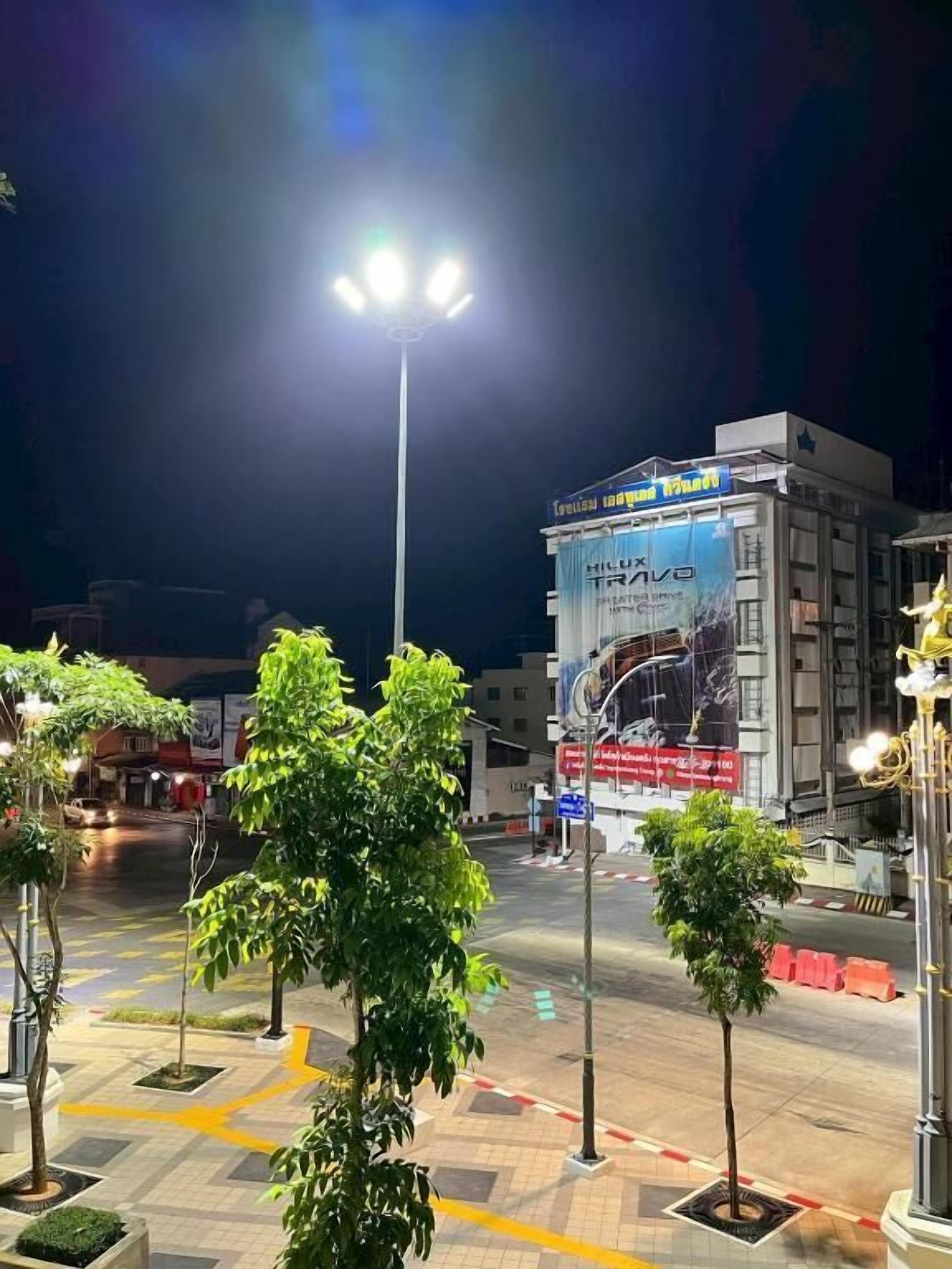 A nighttime urban street scene with a brightly lit street lamp, a building with a large advertisement, and a few trees.
