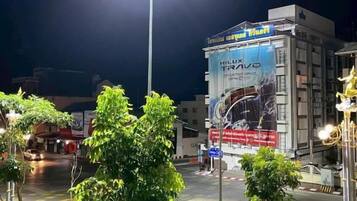 A nighttime urban street scene with a brightly lit street lamp, a building with a large advertisement, and a few trees.