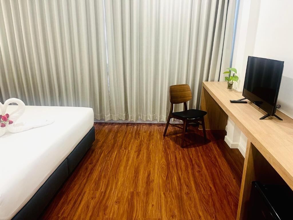 A hotel room with a bed, a desk with a TV, a chair, and a plant.