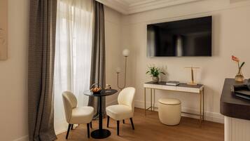 Een moderne hotelkamer met een eethoek, een flatscreen televisie, een tafeltje met een plant en een zithoek.