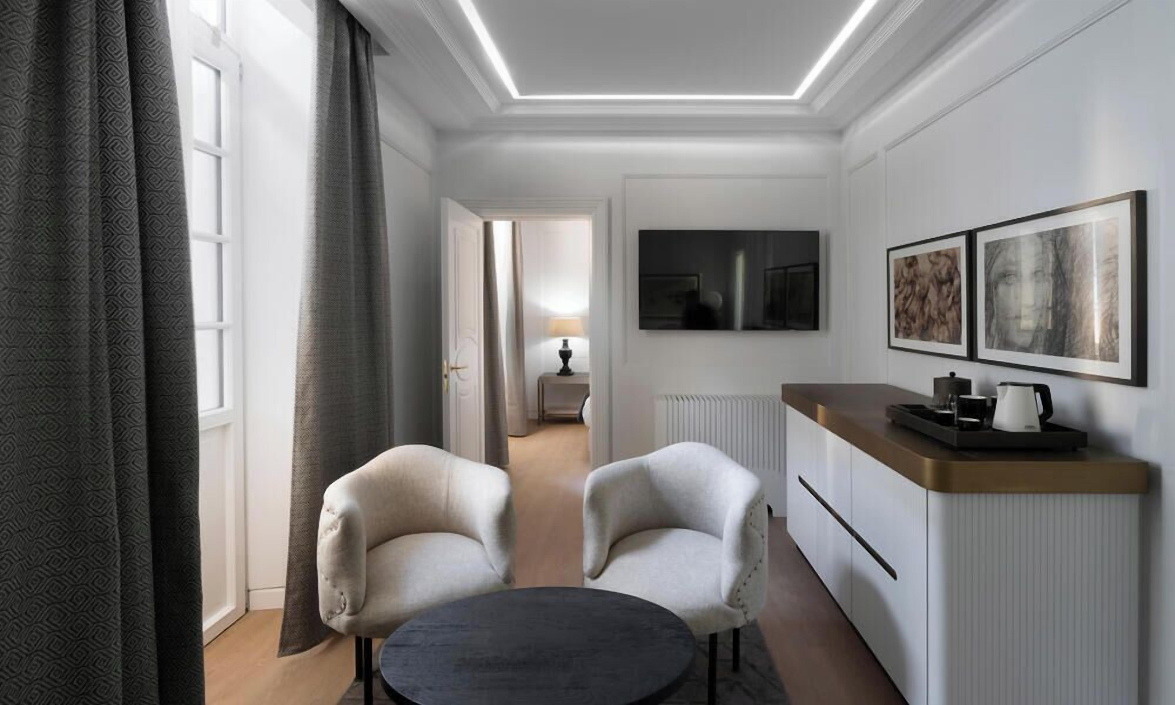 Une chambre d’hôtel moderne comprenant un coin repas, deux fauteuils, une petite table, un téléviseur et des œuvres d’art accrochées au mur.