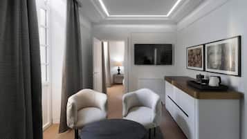 Une chambre d’hôtel moderne comprenant un coin repas, deux fauteuils, une petite table, un téléviseur et des œuvres d’art accrochées au mur.