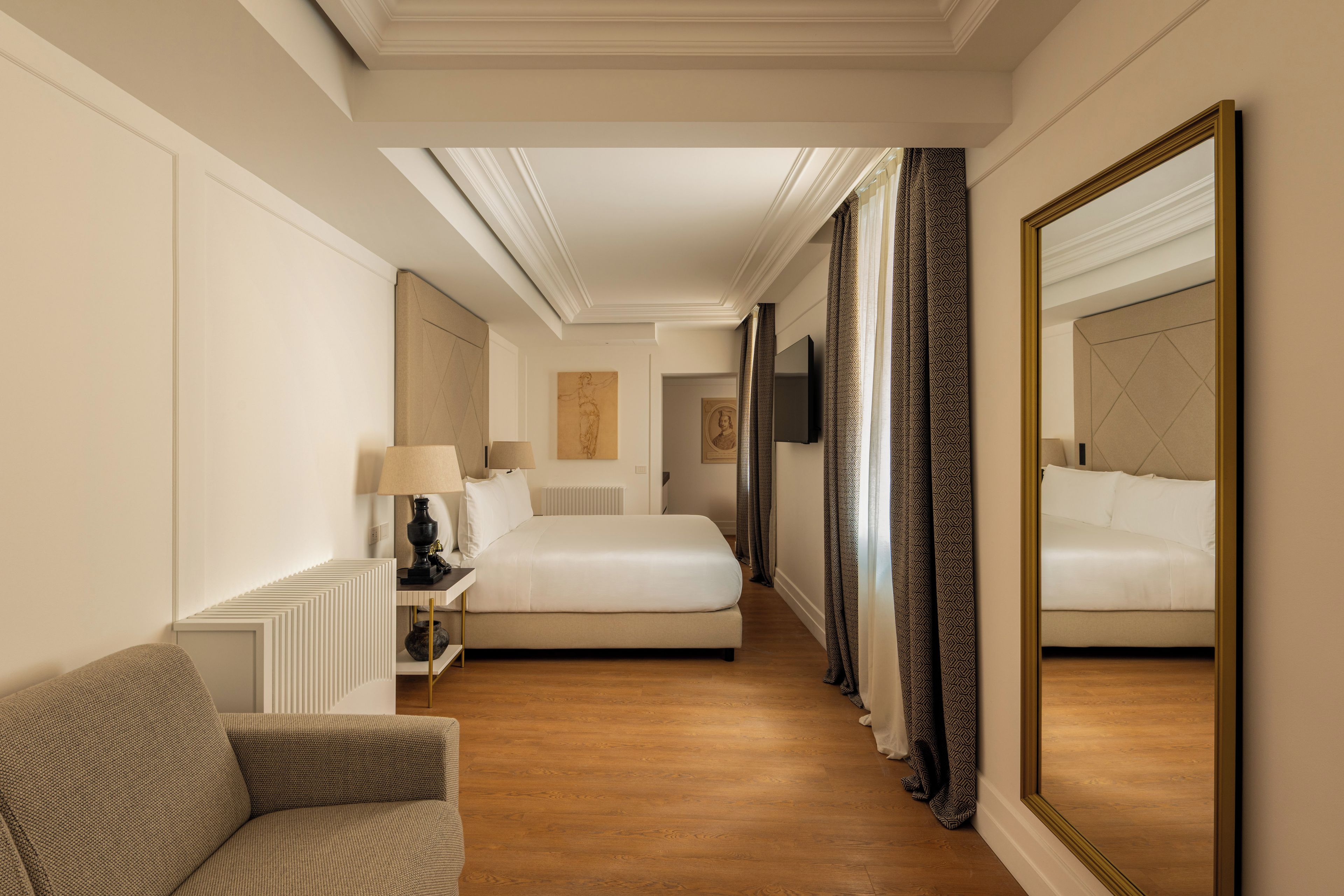 Une chambre d’hôtel avec un grand lit, un coin salon avec un fauteuil, un bureau et un grand miroir.