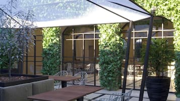 Un espace extérieur aménagé avec des tables et des chaises, entouré de verdure et protégé par une paroi de verre.