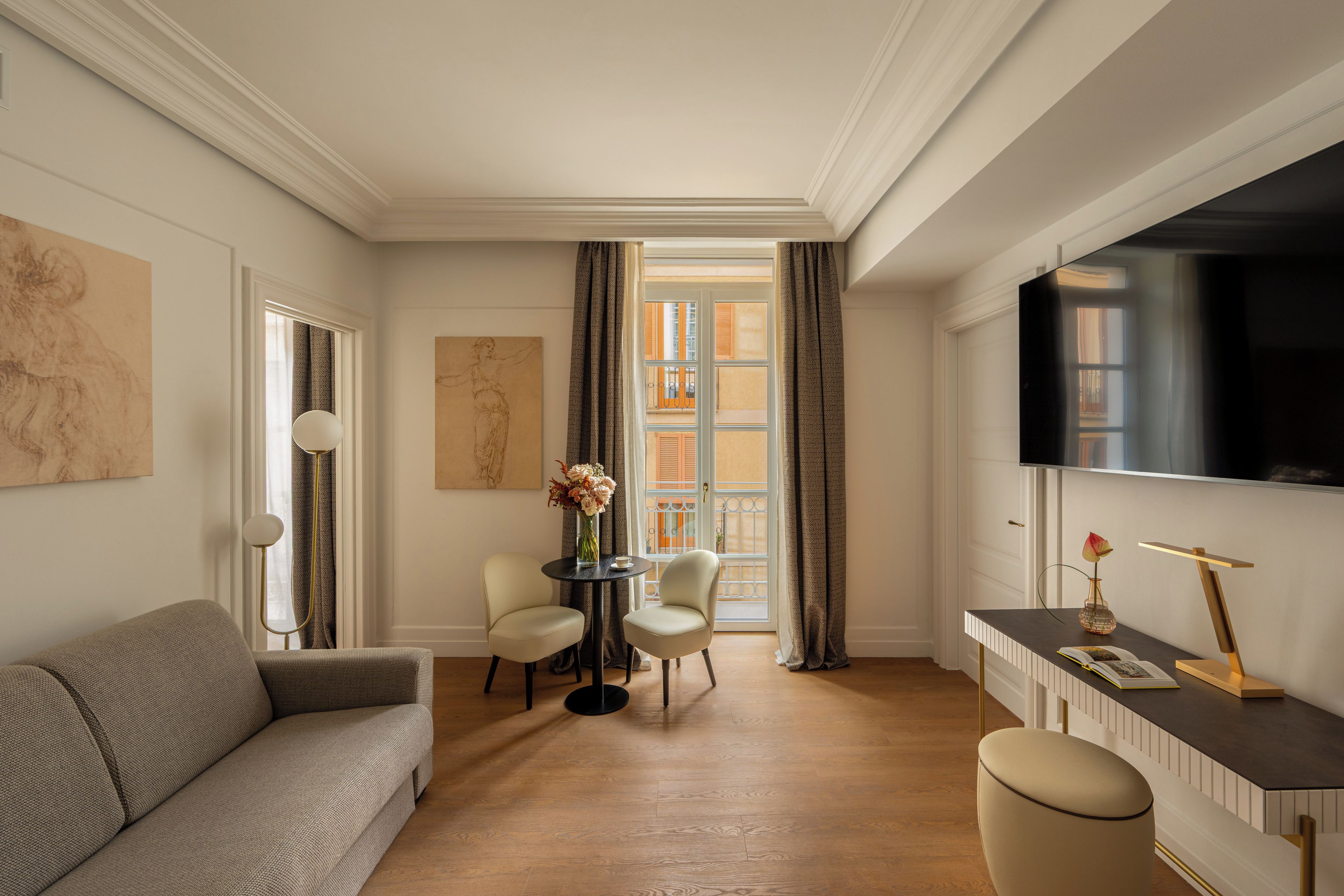 Ein modernes Wohnzimmer mit einer Couch, einem runden Tisch mit Stühlen, einem Fernseher und einem großen Fenster mit Vorhängen.