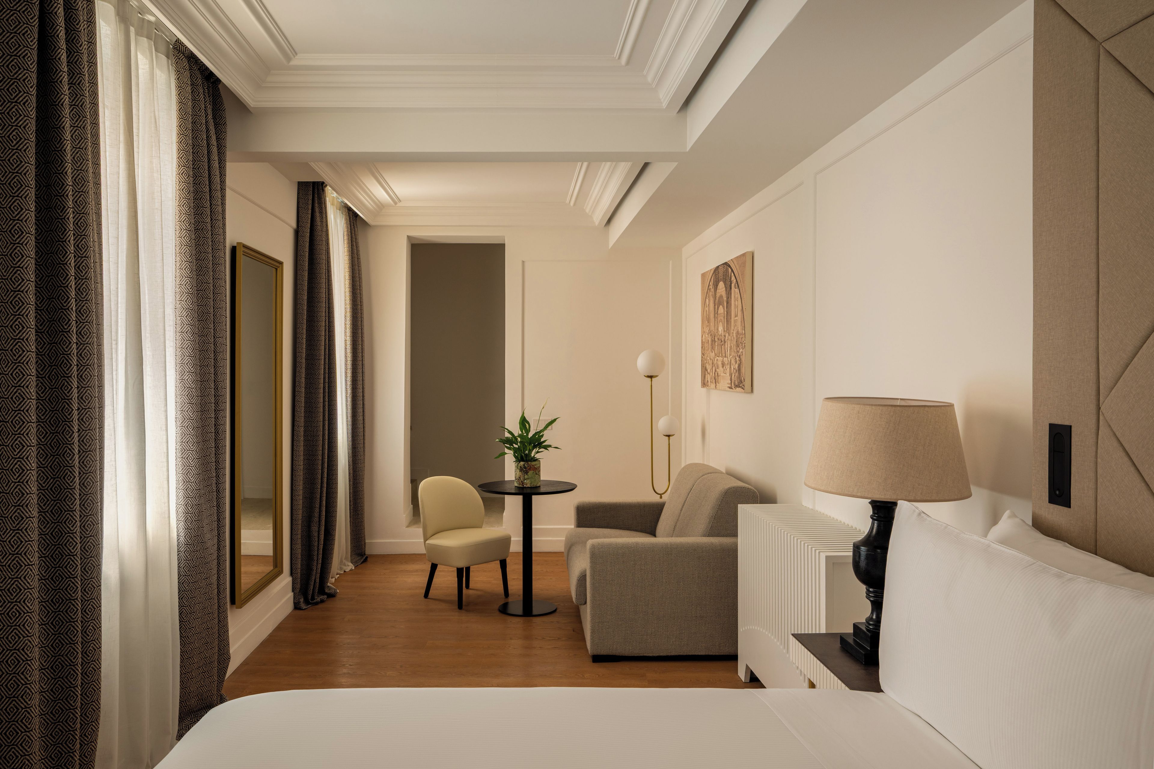 Ein Hotelzimmer mit Bett, Schreibtisch, Stuhl, Tisch mit Pflanze und Lampe.