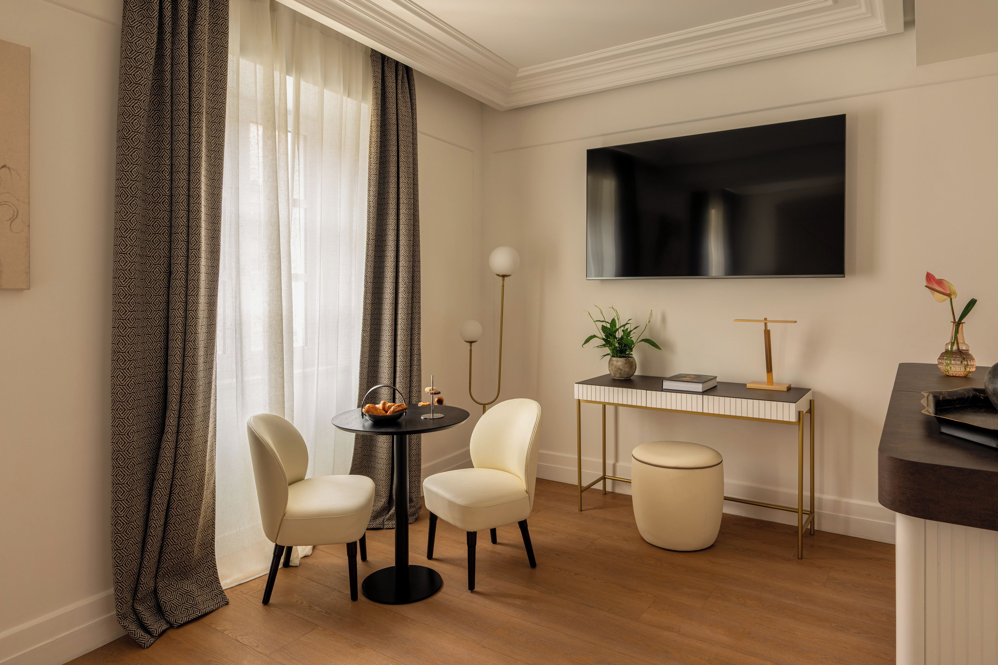 Una habitación de hotel moderna con zona de comedor, televisión de pantalla plana, una mesita con una planta y un conjunto de asientos.