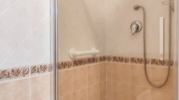 Un espace douche doté d’une porte en verre, d’un pommeau de douche à main et de commandes fixées au mur.