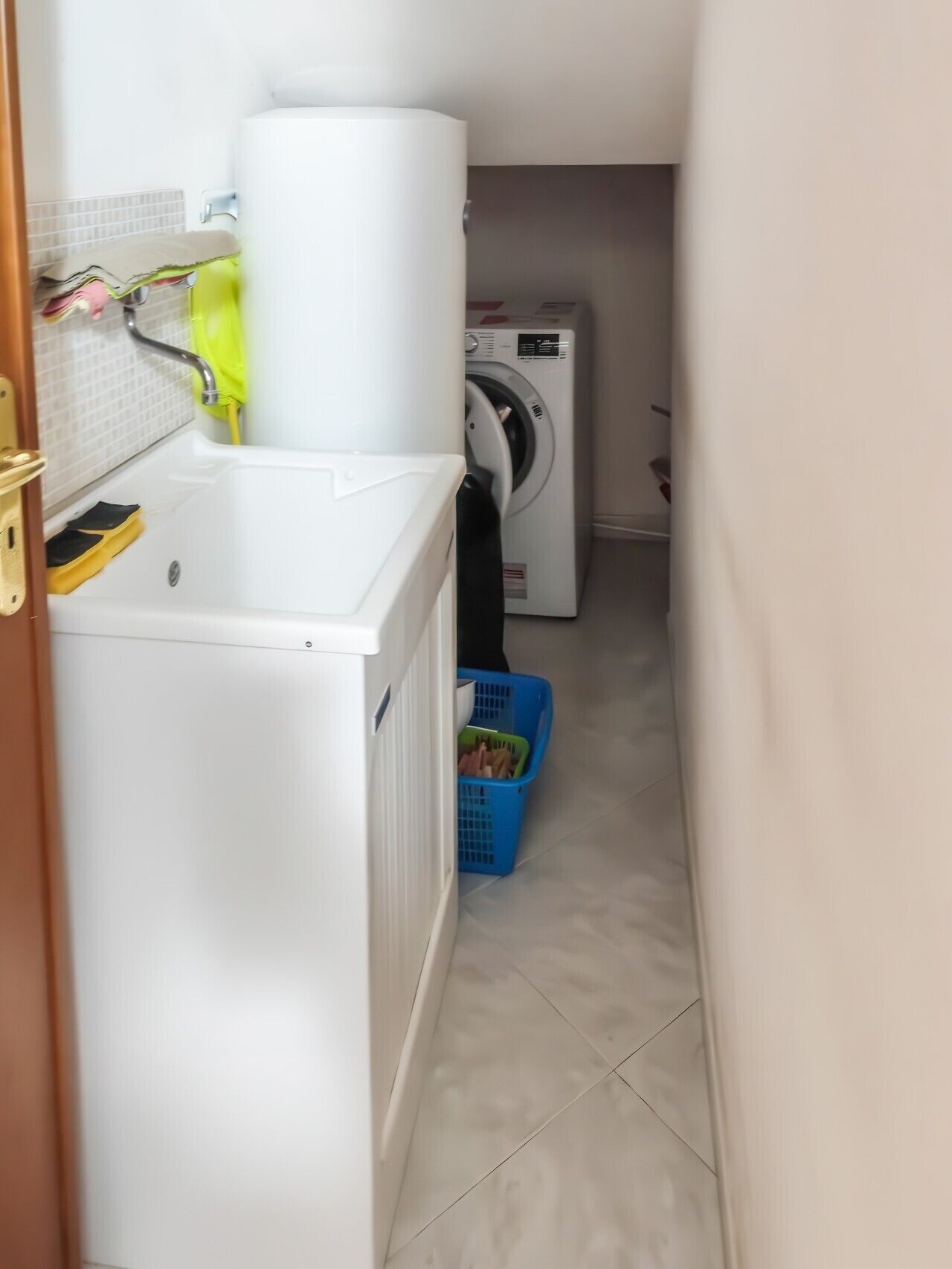Une buanderie équipée d’un lave-linge et d’un sèche-linge à chargement frontal, d’un panier à linge bleu et d’une serviette jaune accrochée au mur.