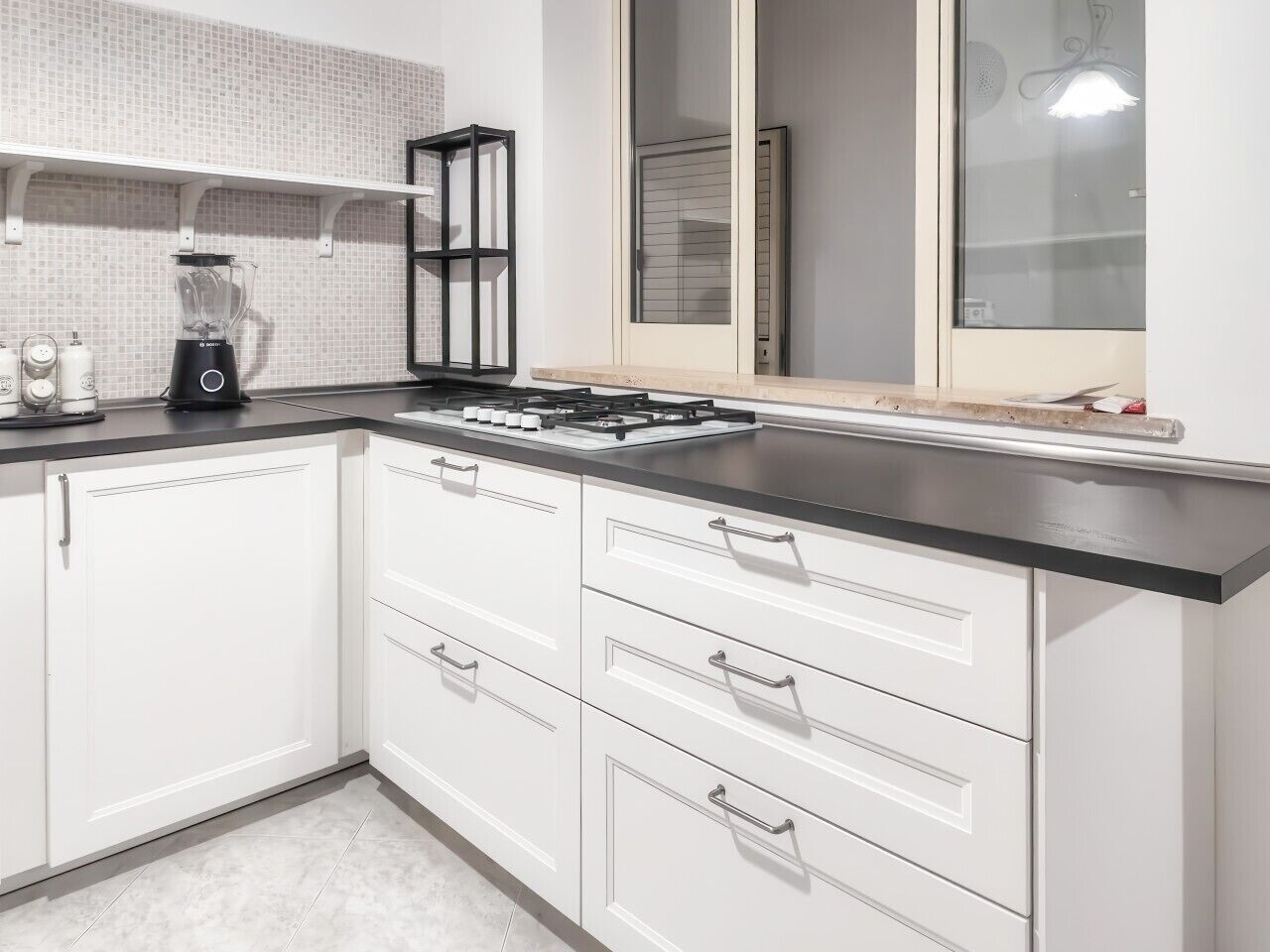 Una cocina moderna con armarios blancos, encimera negra y estufa integrada.