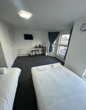 A hotel room with two beds, a desk, a chair, a TV, and a window with curtains. - Kent Hotel (Great Yarmouth)