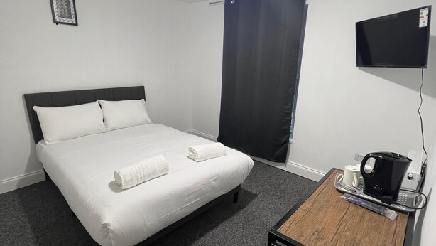 Una habitación de hotel con una cama, un escritorio con cafetera y un televisor de pantalla plana.
