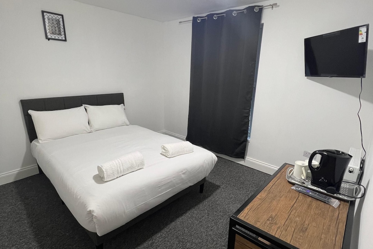 A hotel room with a bed, a desk with a coffee maker, and a flat-screen TV.