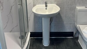 Un baño con cabina de ducha de vidrio, un lavamanos pedestal y un inodoro.