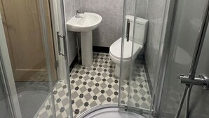 Un baño pequeño con cabina de ducha de vidrio, un lavamanos y un inodoro.