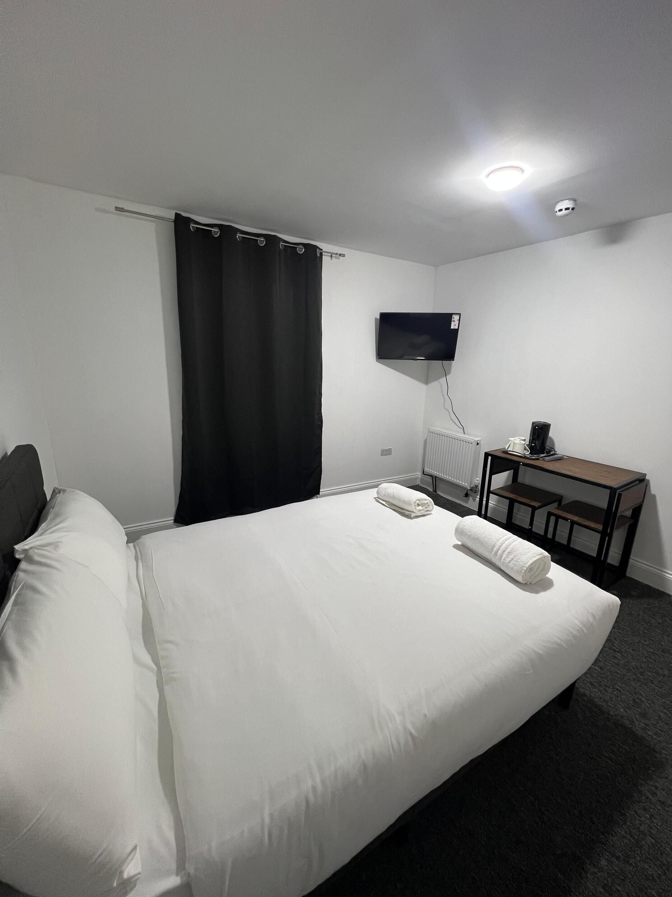 Habitación de hotel con cama, escritorio, televisión y ventana con cortinas.