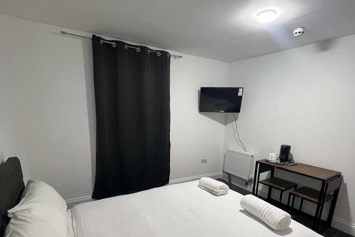 A hotel room with a bed, a desk, a television, and a window with curtains.