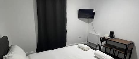 Ein Hotelzimmer mit Bett, Schreibtisch, Fernseher und einem Fenster mit Vorhängen.