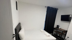 Una habitación pequeña con cama individual, escritorio y televisor.