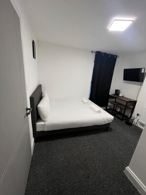 Una habitación pequeña con cama individual, escritorio y televisor.