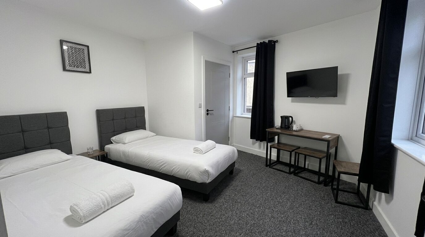 Habitación de hotel con dos camas, un escritorio, un televisor y un ventanal con cortinas.