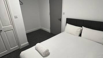 A hotel room with a bed, a door, a clock, and a framed picture on the wall.