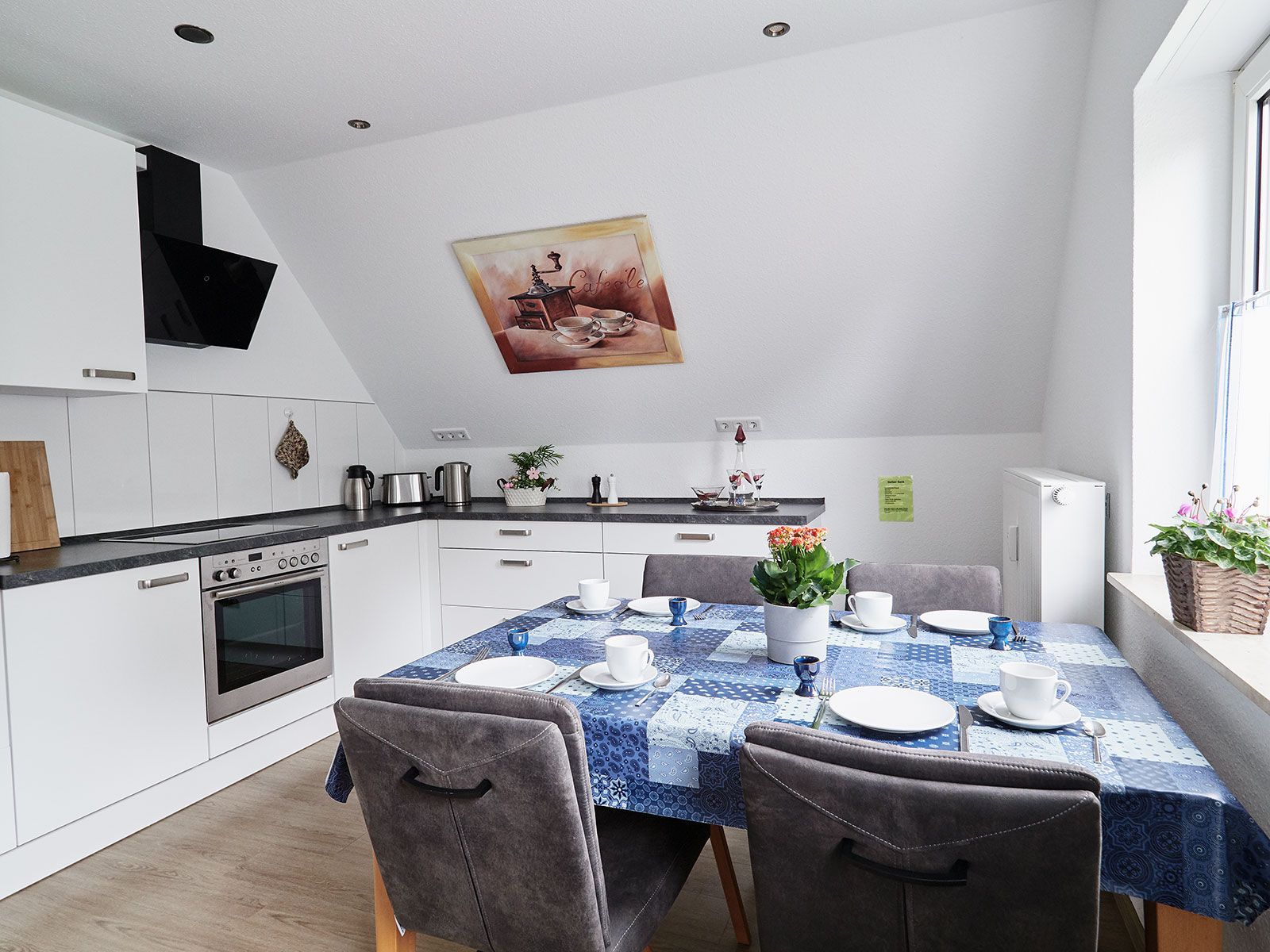 A modern kitchen with white cabinetry, a built-in oven, and a dining area with a blue tablecloth.