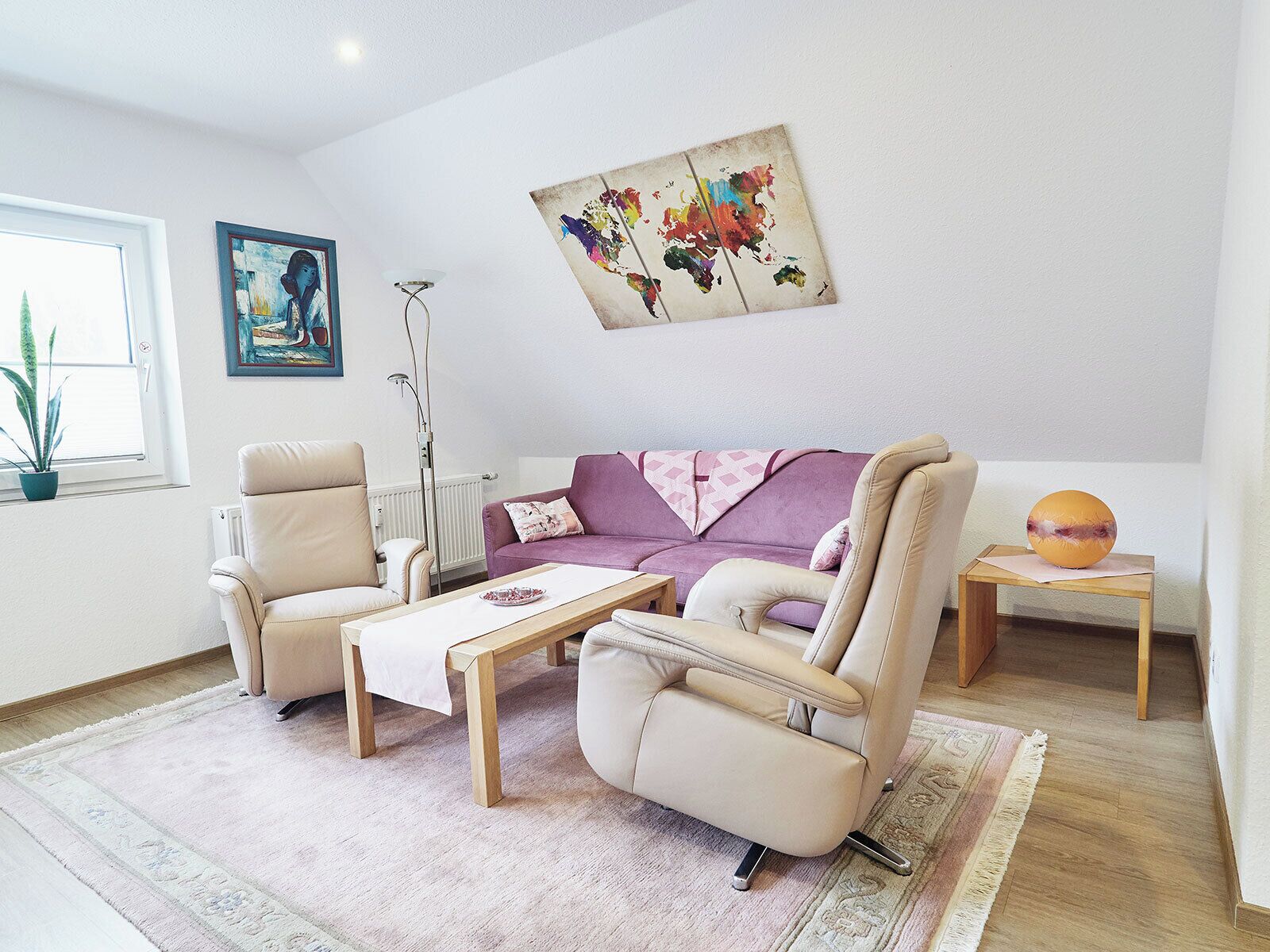A living room with a sofa, two armchairs, a coffee table, a floor lamp, a painting, and a small table with a fruit.