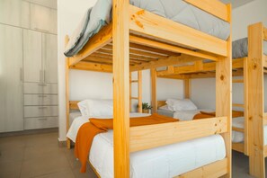 A bunk bed room with a wooden frame, white bedding, and a grey pillow.
