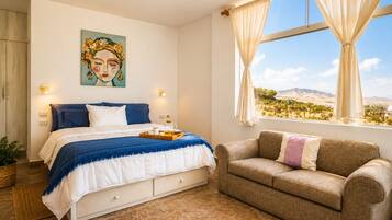 Un dormitorio con cama, sofá, un cuadro y ventana con vistas.