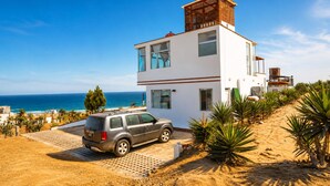 A modern two-story house with a car parked in front, located near a beach with clear skies.