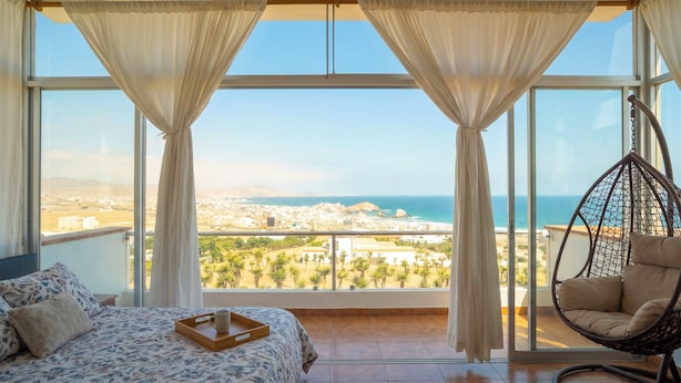 A bedroom with a large window, a hanging chair, and a bed with a tray.